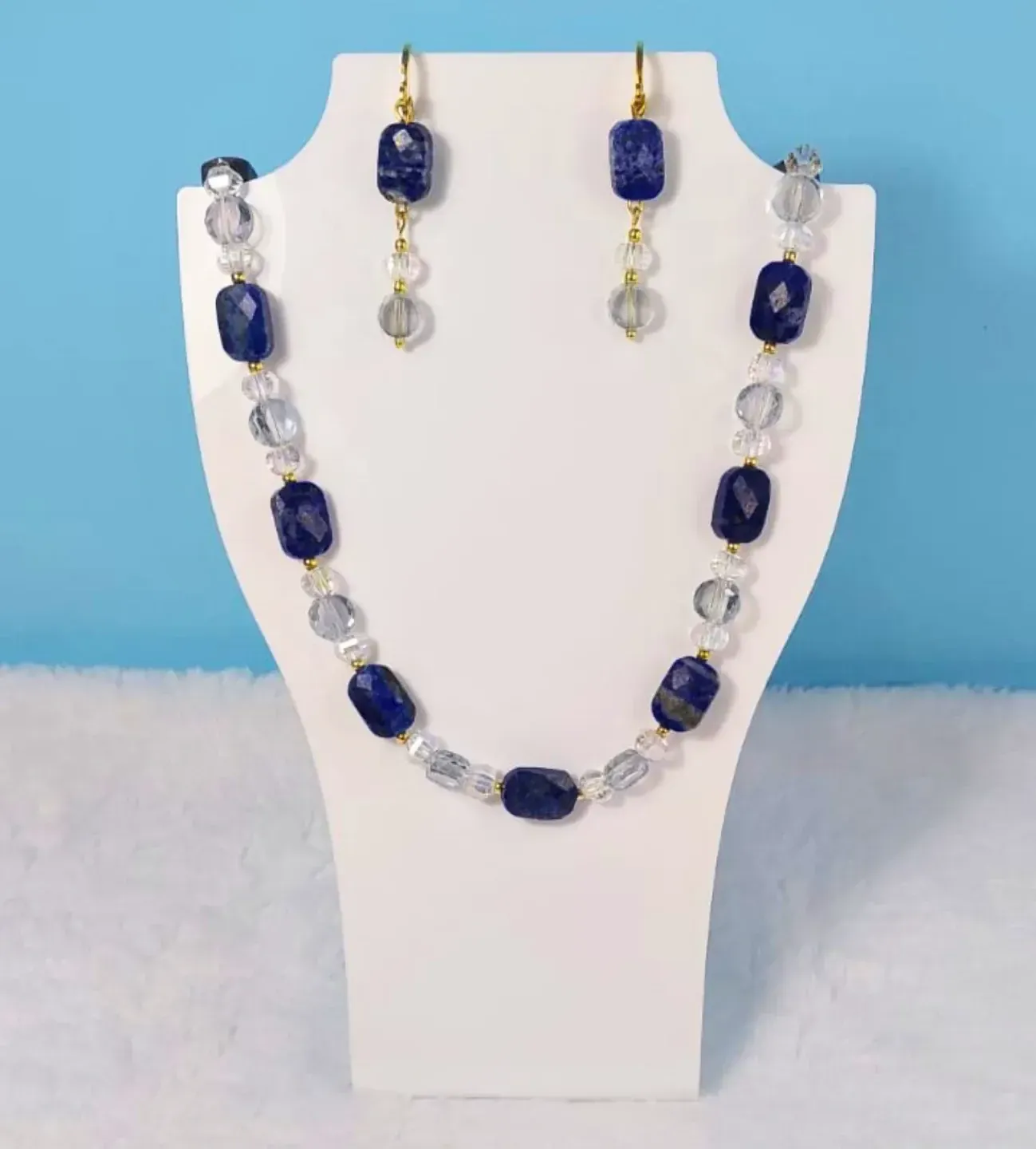 Colar de pedras azuis facetadas e cristais com brincos combinando, exposto em um busto branco