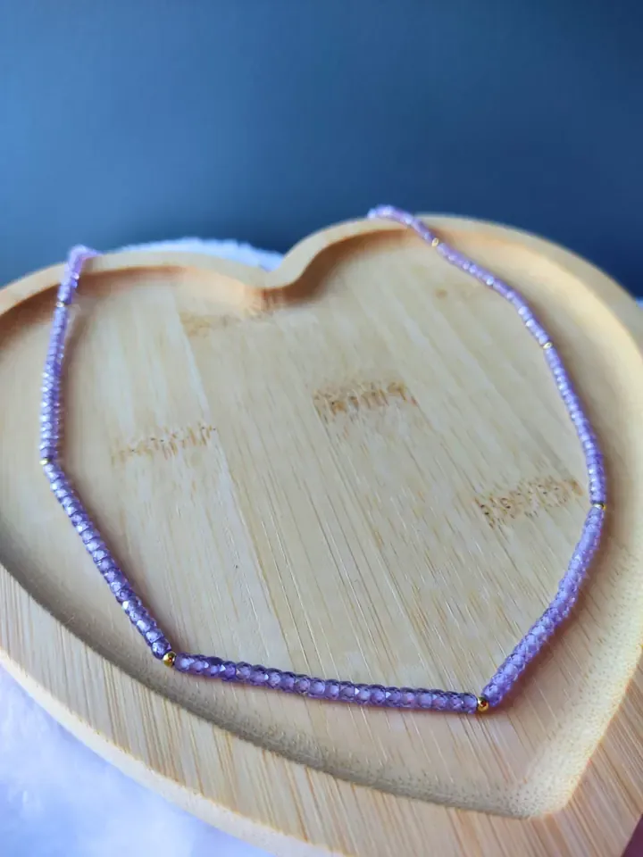 Choker de pequenos cristais lilás facetados sobre bandeja de madeira em formato de coração