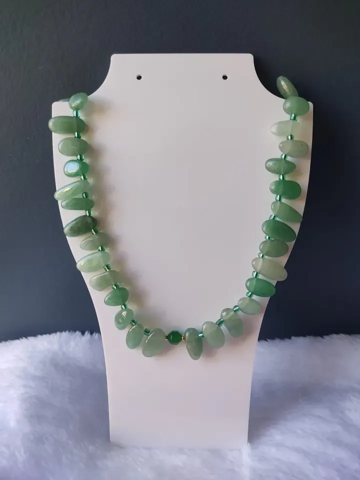 Colar de pedras verdes em formato de gota exposto em um busto branco
