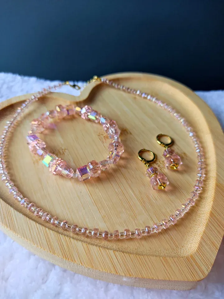 Colar, pulseira e brincos de cristais rosa furta-cor sobre bandeja de madeira em formato de coração