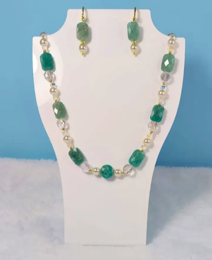 Colar de pedras verdes facetadas, pérolas e cristais, com brincos combinando, em um busto branco