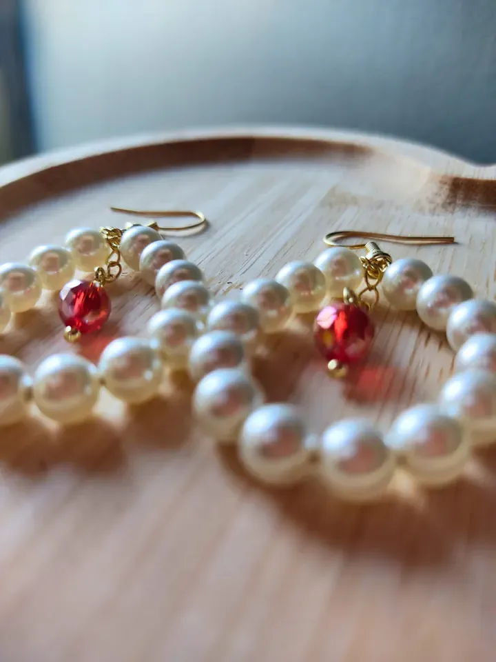 Fio de pérolas grandes e brincos de pérolas com cristal vermelho facetado, sobre madeira