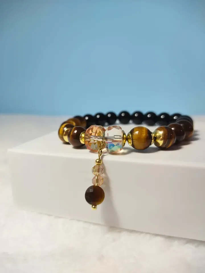 Pulseira de olho de tigre e contas pretas com cristais champanhe e pingente, sobre uma caixa branca