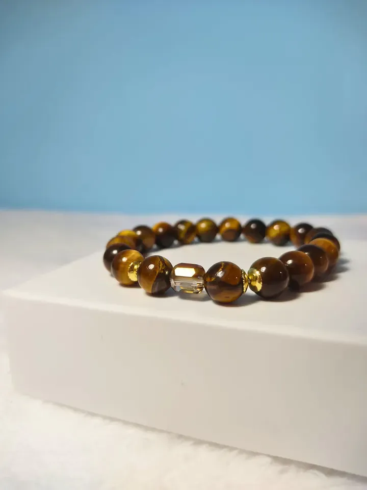 Pulseira de contas marrom-douradas de olho de tigre com cristal facetado, sobre uma caixa branca